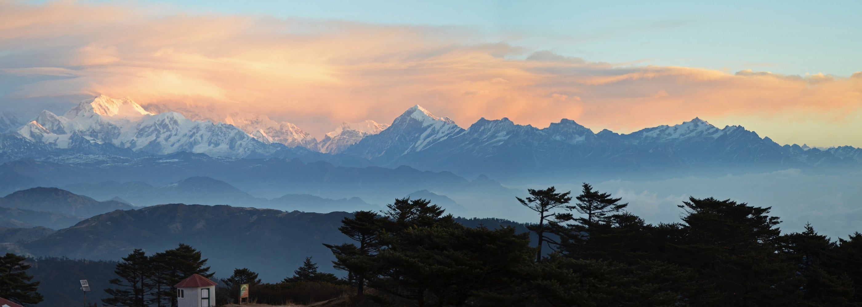 The Kangchenjunga range in the Himalayas at dusk, seen across forested hills